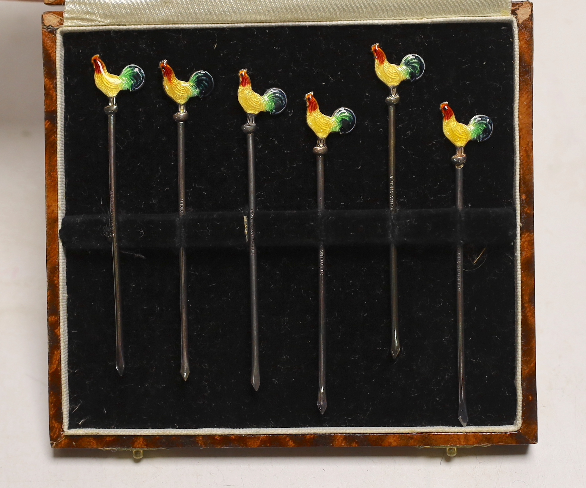 A cased set of six sterling and enamel cocktail sticks, with cockerel terminals and three silver napkin rings.